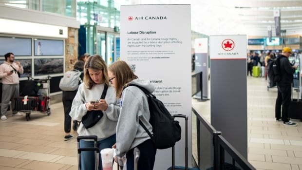 People wait at an Air Canada check in at Vancouver International Airport in Richmond, B.C., on Sunday, Aug. 17, 2025. Air Canada made the call to halt a return to operation as flight attendants continue to strike. THE CANADIAN PRESS/Ethan Cairns People check their cellphones while standing with their luggage inside an airport.