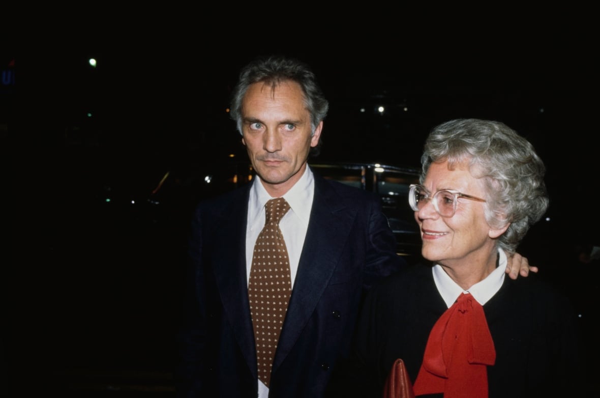 A white-haired man in a suit and tie and an older woman with white hair are shown in a nighttime photo.
