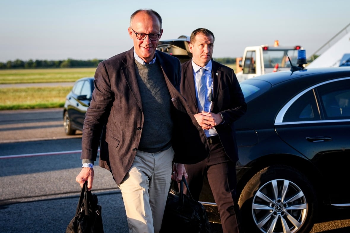 A man with glasses, Bang, and Shavin style appear walking near a car. Part of a plane appears.
