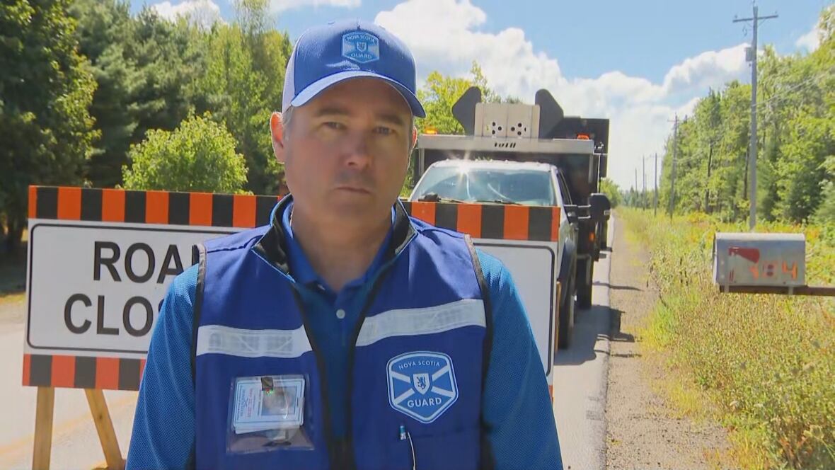 Man in blue shirt and hat is near a plate with the "road closed".