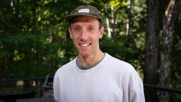 A smiling man wearing a light grey sweater and green cap.