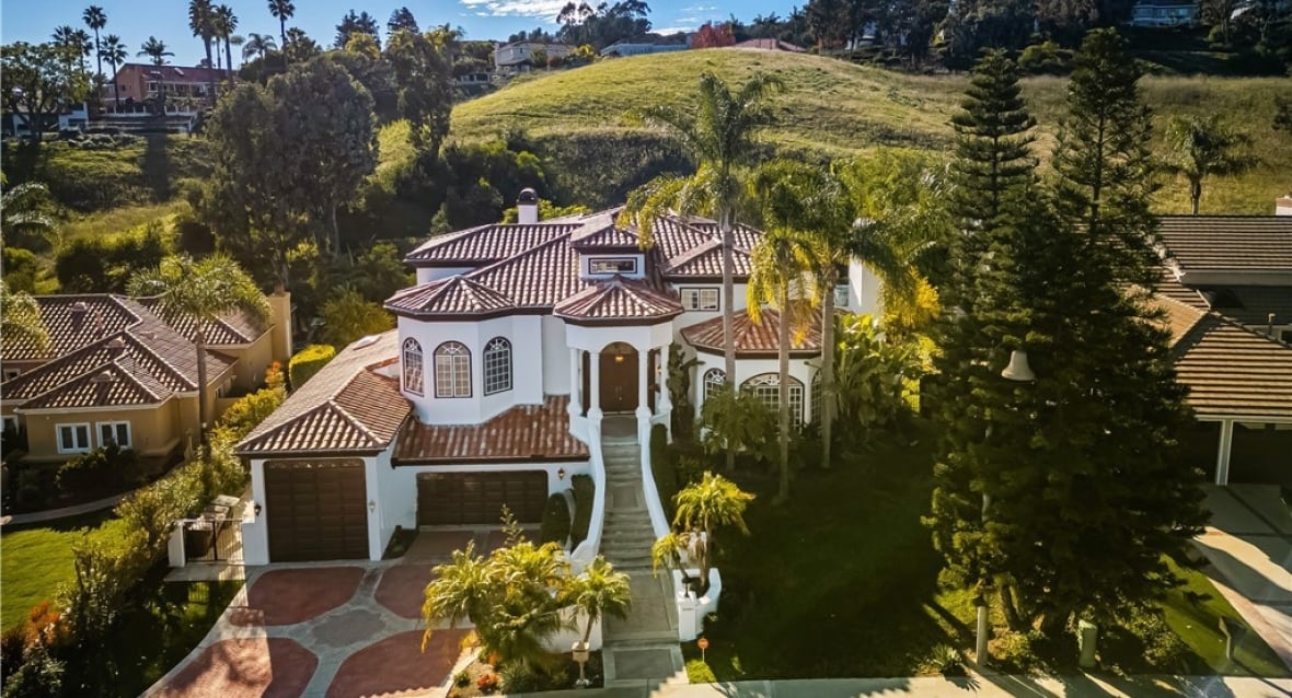 A mansion with a white facade. It has palm trees in its front yard.
