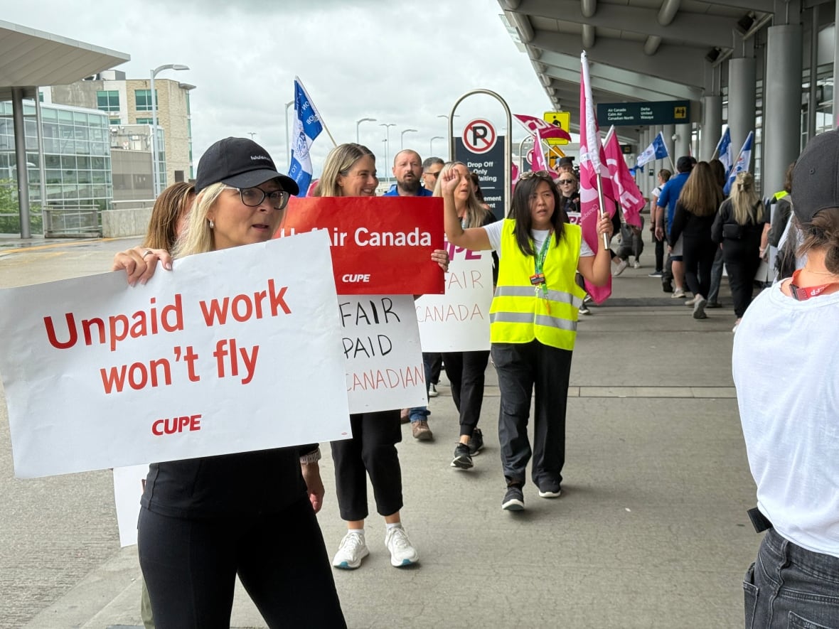 A row of people on strike walk in circles on the picket line. A woman holds up a sign that reads, 'Unpaid work won't fly.'