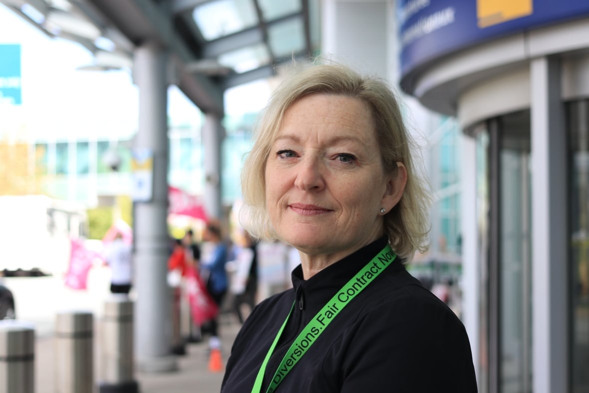 A woman laughs outside an airport. Behind her is a picket line.