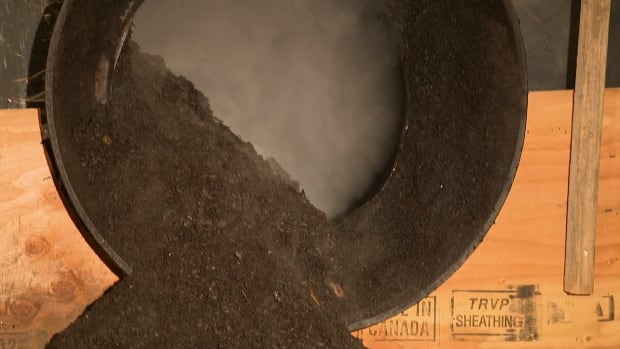 The composter on Salt Spring Island is meant to take in 60 tonnes of organic materials a year and produce close to 200 metres of compost. A large black tube with dark earth spilling out and steam being emitted.