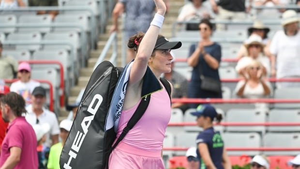 A female tennis player raise one arm up in the air to wave to the crowd on the tennis court.