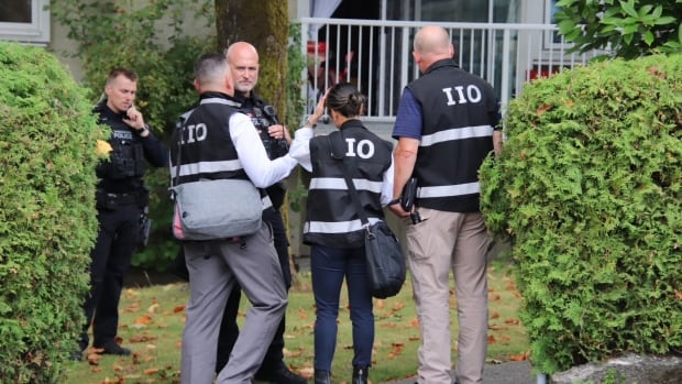 People wearing vests reading 'IIO' are seen speaking to police outside a housing block.