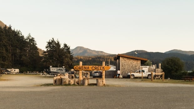 The campground and marina at China Creek near Port Alberni, B.C., is no longer under evacuation order as of Aug. 20, 2025, but remains under evacuation alert. A sign says China Creek with a building and a lake in the background.