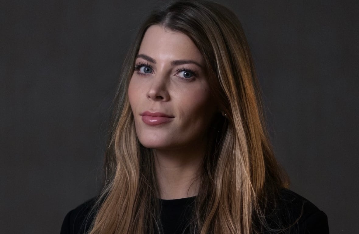 A woman in a black top poses for a potrait, against a grey backdrop.