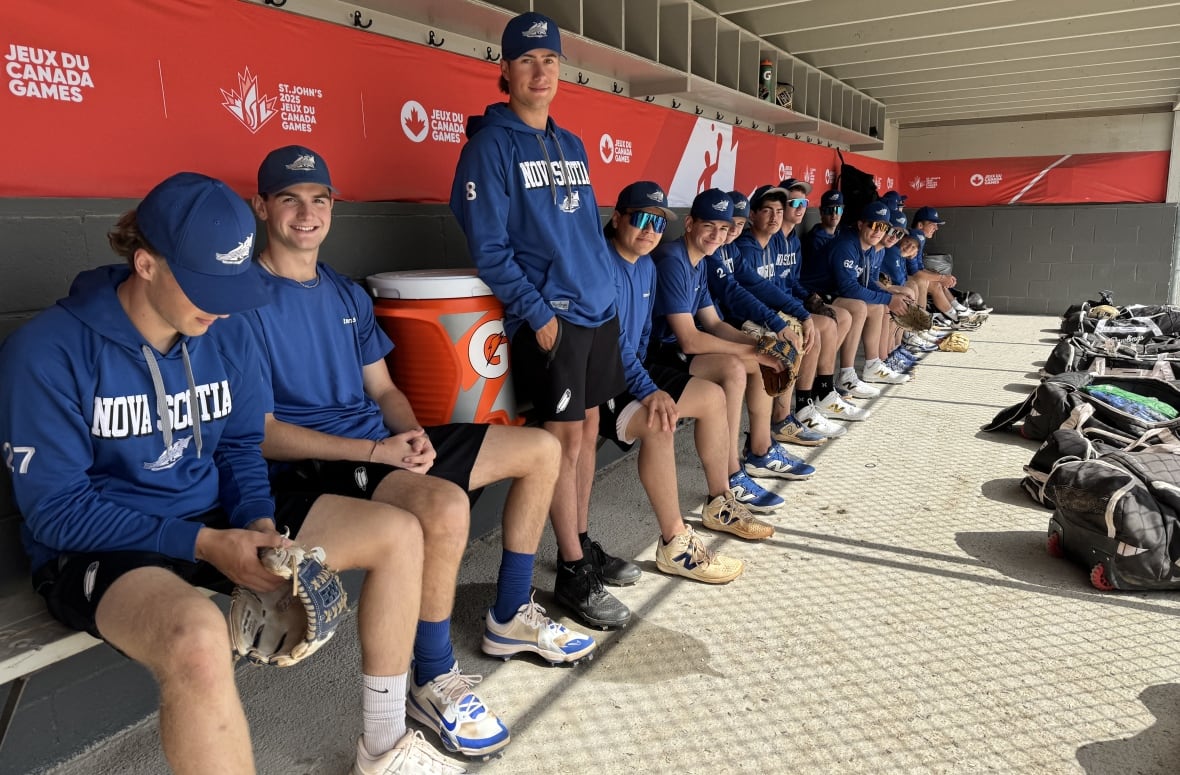 A softball team is seen sitting in the dugout. 