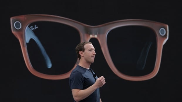 A man stands in front of a large screen showing glasses.