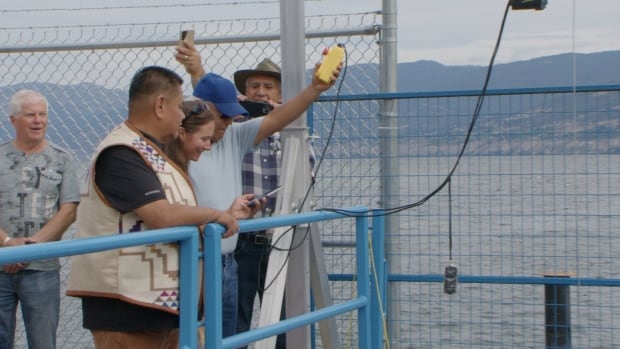 PIB Chief Greg Gabriel and Zoe Eyjolfson opening the fish passageway for the first time on Aug. 18, 2025. People gather holding a button that opens the new fish passageway.