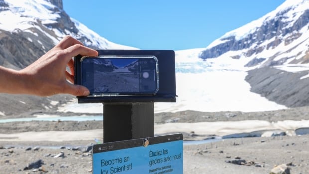 A hand is using a cellphone to take a photo of a glacier.