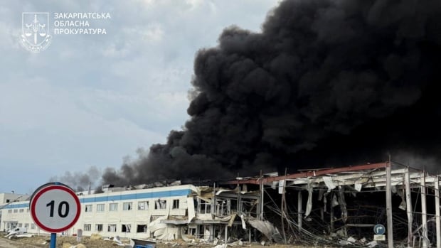 A long, low-rise building is shown to have suffered heavy destruction, with large clouds of black smoke shown.
