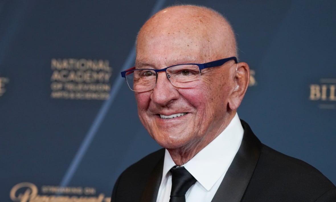 A man appears wearing a shoulder suit. He smiles and contains glasses. 