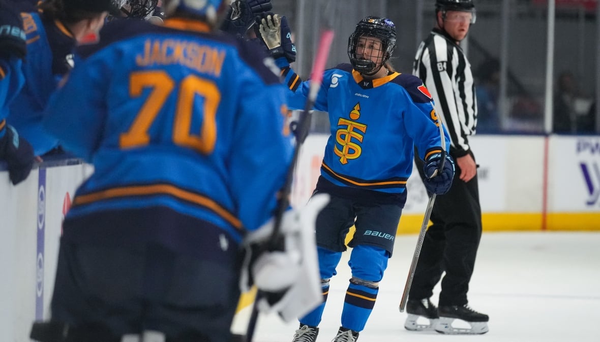 A hockey player wearing a Toronto Sceptres jersey celebrates a goal with her teammates on the bench.