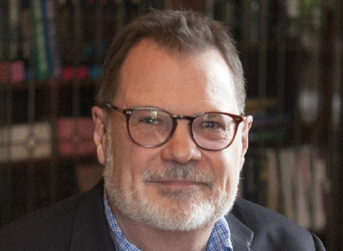 A man with glasses and a gray smile while putting a picture. 