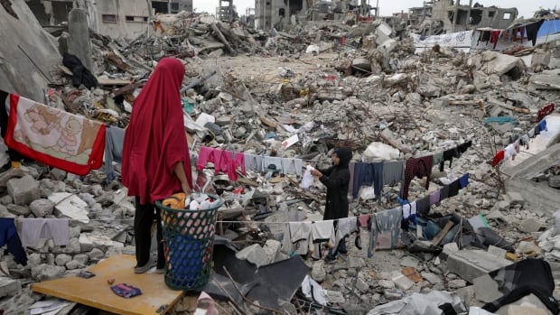 People hang laundry in rubble.
