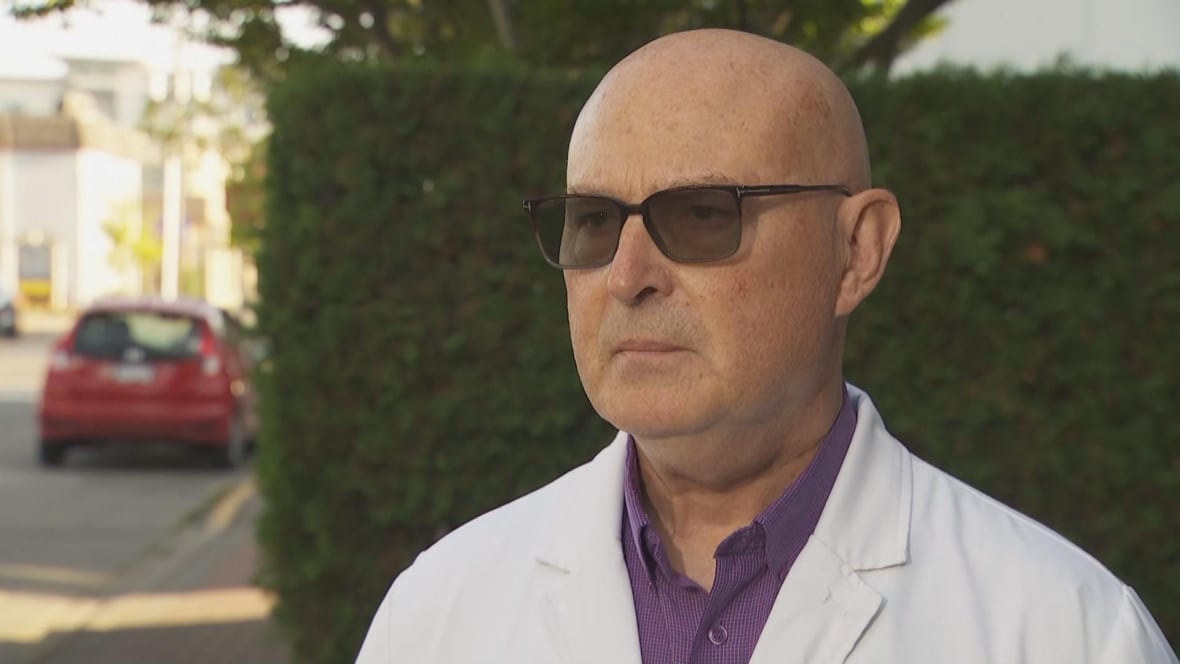 A man in a lab coat and sunglasses speaks to a camera