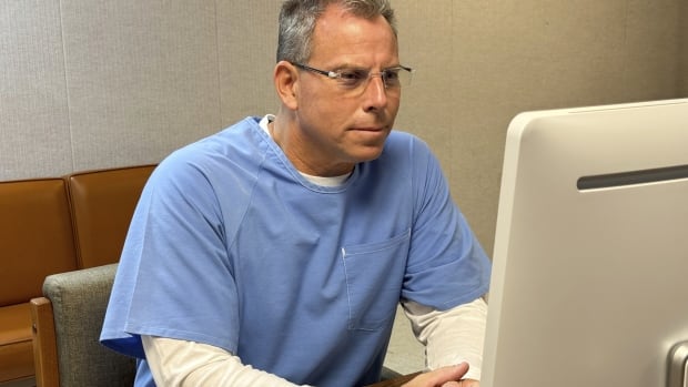 Erik Menendez appears before the parole board via teleconference on Thursday, Aug. 21, 2025, at the Richard J. Donovan Correctional Facility in San Diego. A man in a blue jumper sits in front of a computer.