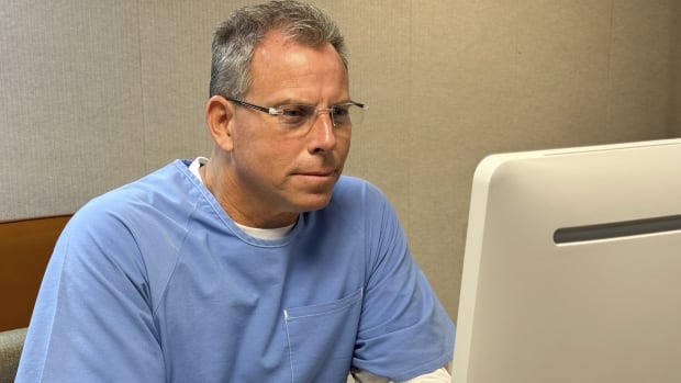 A man in a blue jumper sits in front of a computer.