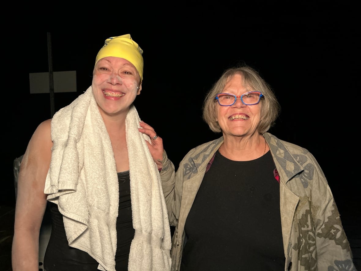 A woman in a swimsuit smiles proudly next to her mother after completing a 50 kilometer swim. 