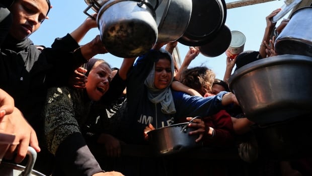 A crowd of people wait to receive food