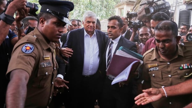 Former Sri Lankan President Ranil Wickremesinghe, center, is escorted in a court by the police in Colombo, Sri Lanka, Friday, Aug. 22, 2025. A man in a suit is escorted by police