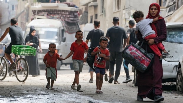A woman walking on a dusty city street is carrying a young child, as three other children follow behind.