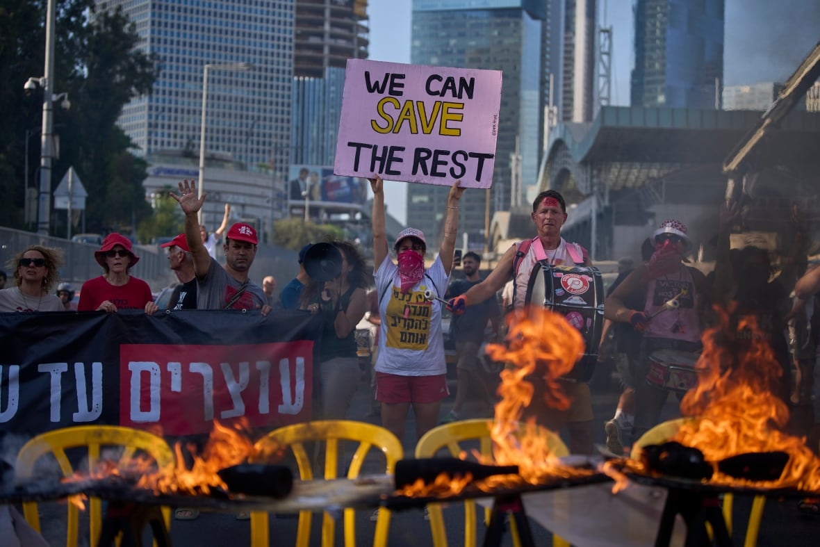 A line of demonstrators is displayed behind a lit table on the fire, with yellow plastic chairs under it. At the center, one person carries a sign of reading: we can save the rest.