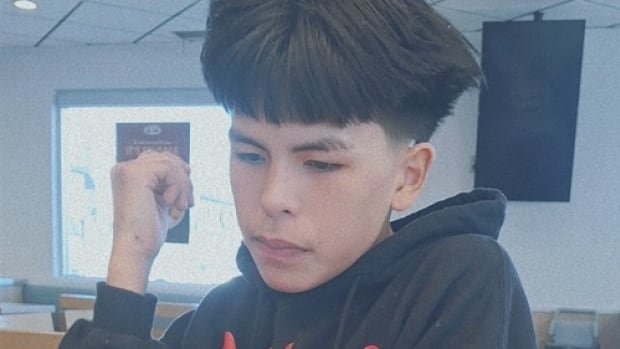 A boy in black hoodie sits at a table.