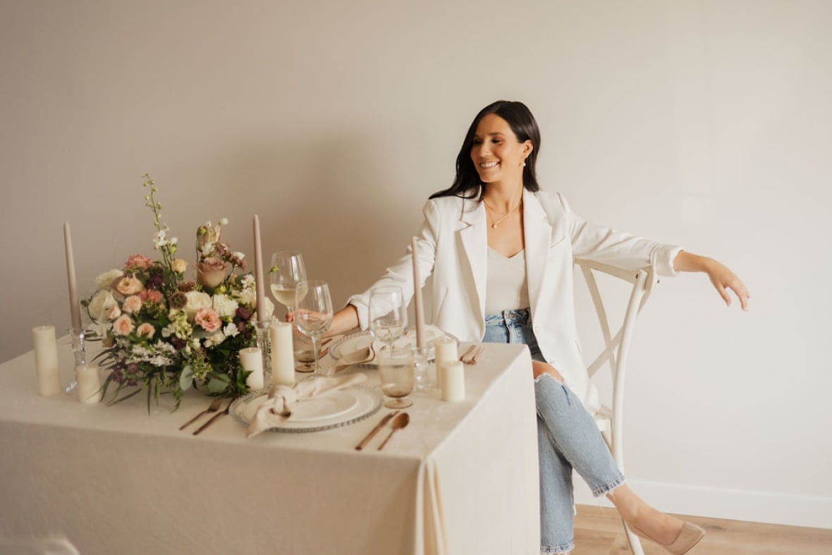 A woman in a white outfit sits next to a decorated wedding table.