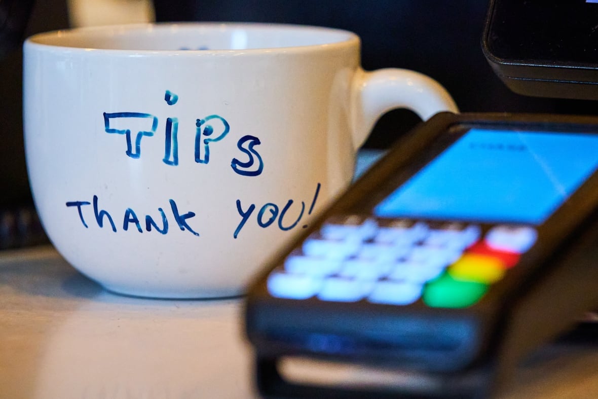 A debit machine sits beside a white mug. Someone wrote, 'Tips, thank you!' on the mug in blue ink.