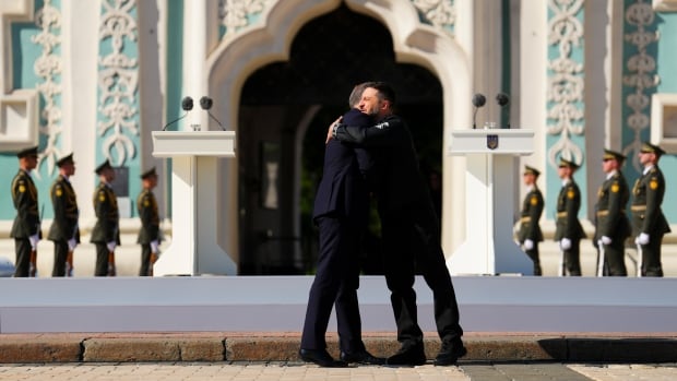 Two men hug in front of an ornate blue and white building.