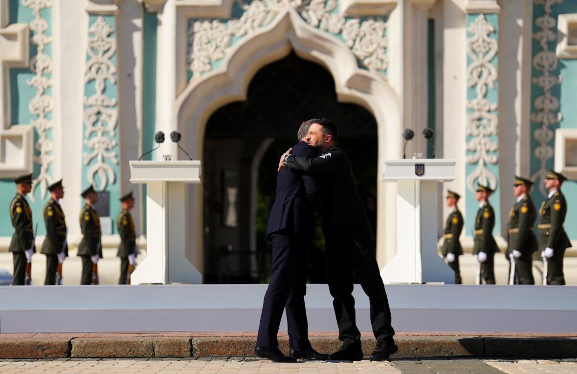 Two men embrace in front of a blue and white building.