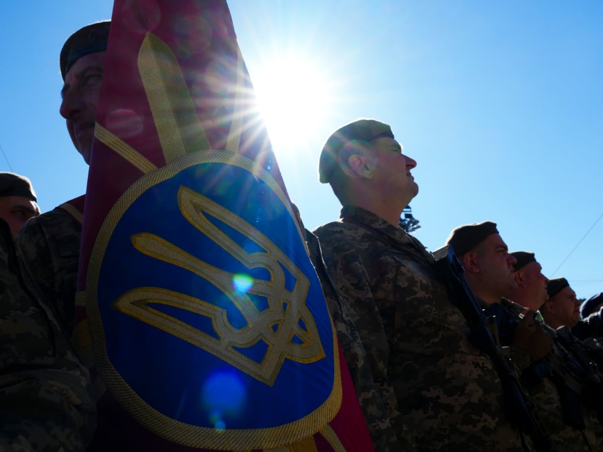 Il sole splende dietro una fila di soldati che reggono una bandiera cerimoniale ucraina.