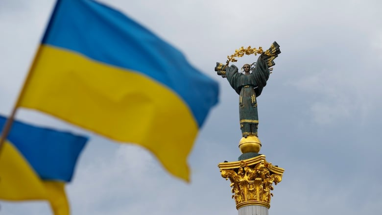 Ukrainian flags blow next to a statue of a woman with gold detailing.