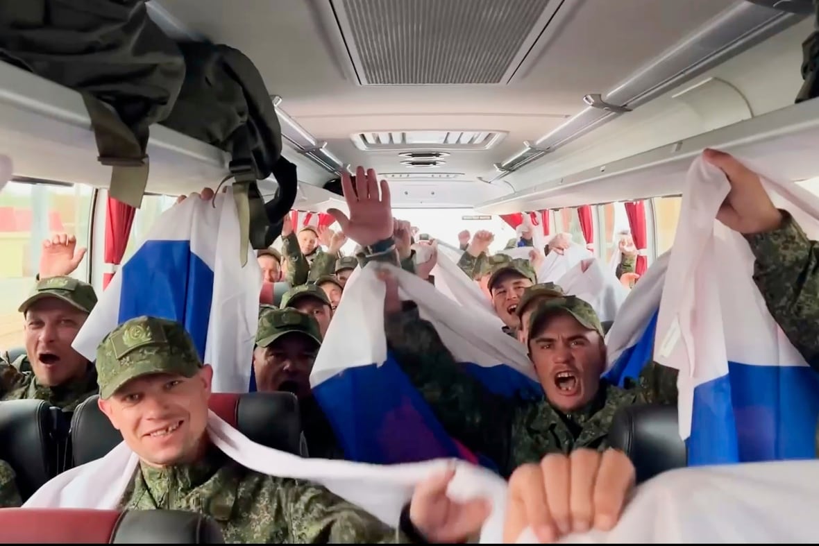 Men in military uniforms wave Russian flags and cheer while sitting in a bus.