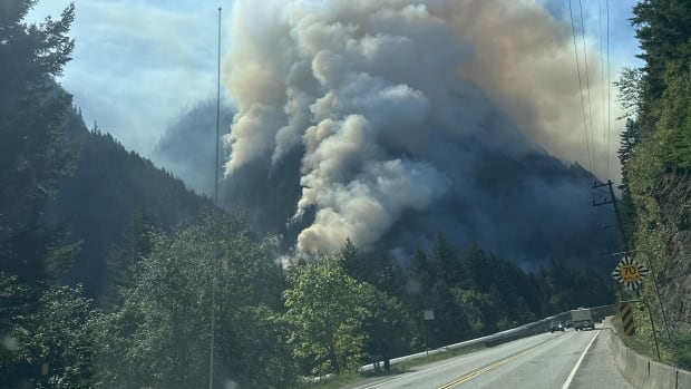 A wildfire burns on a hill on the side of a road with smoke billowing into the air