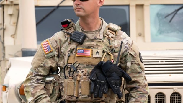 A soldier in uniform is seen standing in front of an armoured vehicle.