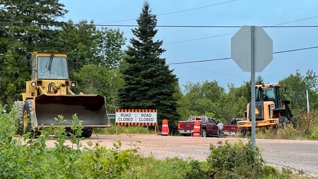 A yellow front-end loader, a 'Road closed' sign and a number of other vehicles are shown.