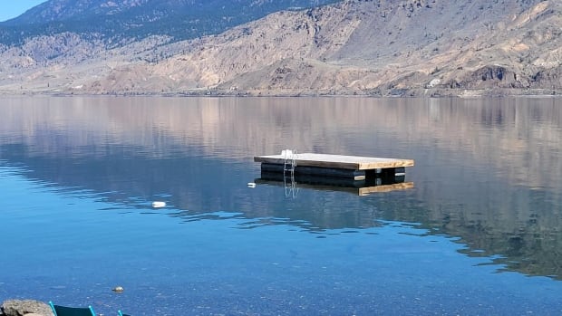 Kamloops Search and Rescue say they recovered a person's body from Kamloops Lake on Saturday, Aug. 23, 2025, after the swimmer failed to make it to a dock. A wooden dock with a ladder floats in a lake with hills in the background and two blue chairs on the shore.
