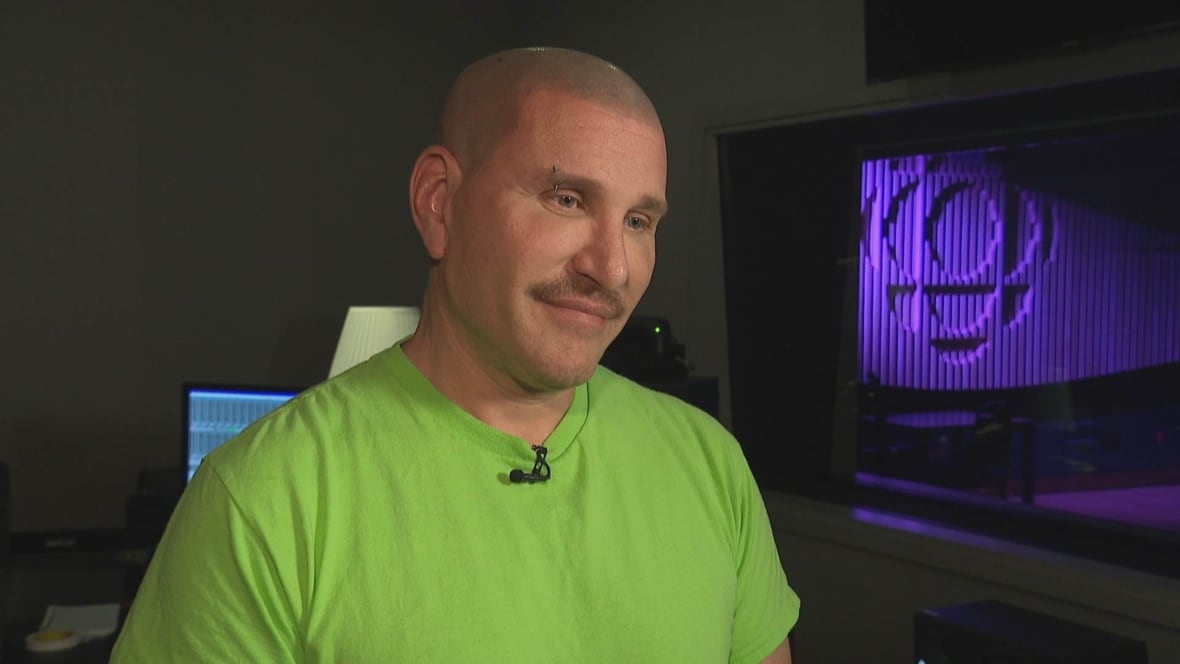 A man in a green shirt and with an eyebrow piercing looks at someone behind the camera.