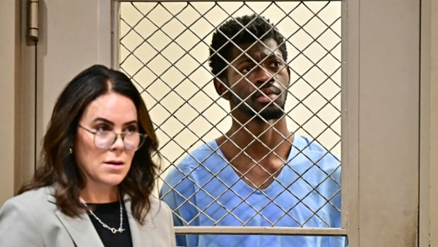 A woman in a suit stands outside of a door with a barred window. On the other side of the window a man in a blue jumpsuit looks on in concern. Below the window is a sign bearing the words 'Do not communicate with prisoners.'