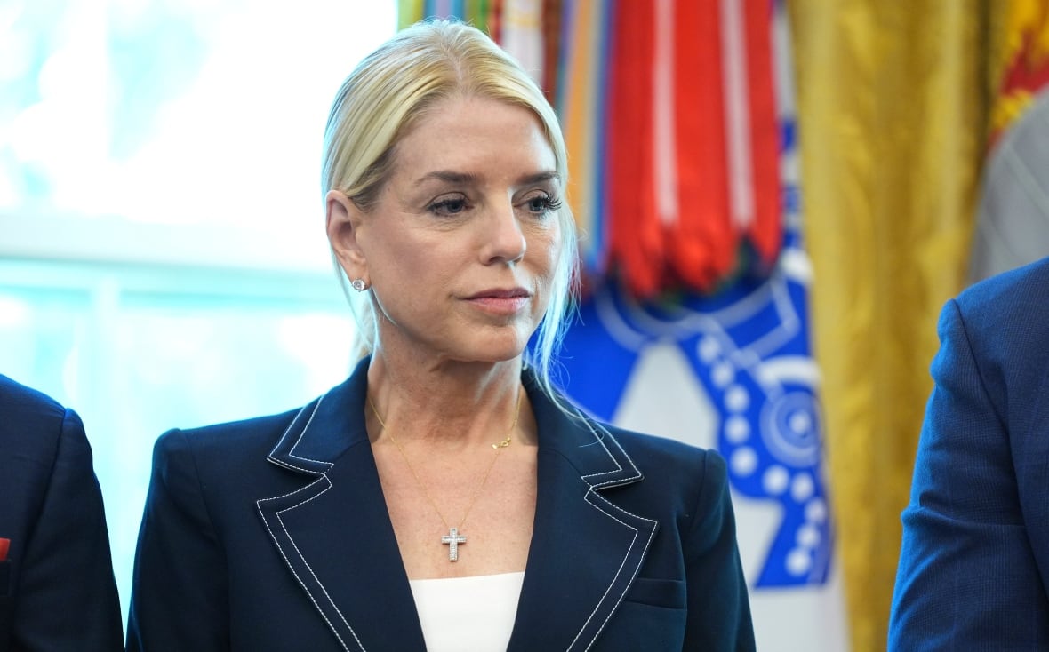 A blond hair woman wears a blue suit standing in front of the flags.