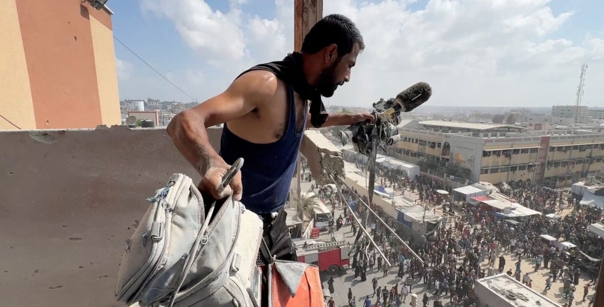 The man holds a camera in one hand and a bag that appeared in the other, both of which are covered with dust, where the crowd looks very much. 