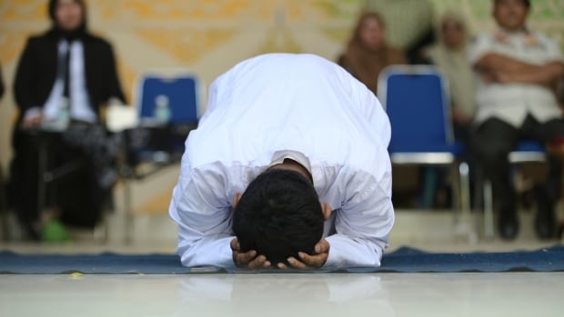 A man in white robes kneels with his head in his hands