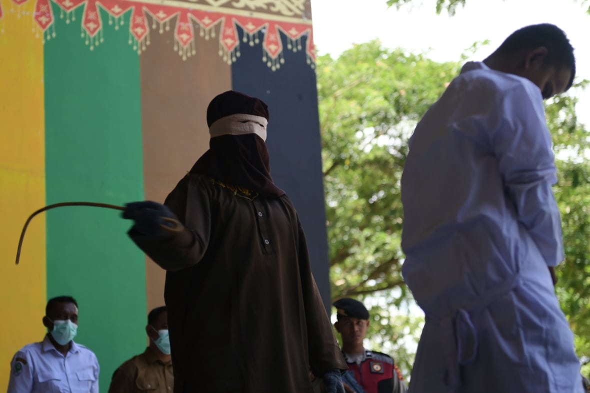 A man wearing a black Jordanian and a mask holding a whip in front of a man wearing a white rose