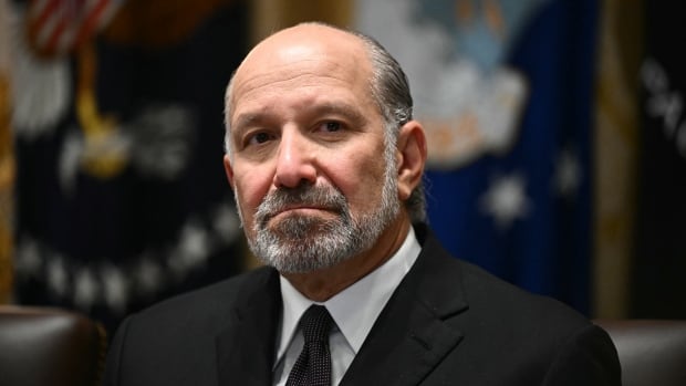 A balding bearded man in a suit and tie is shown in closeup.