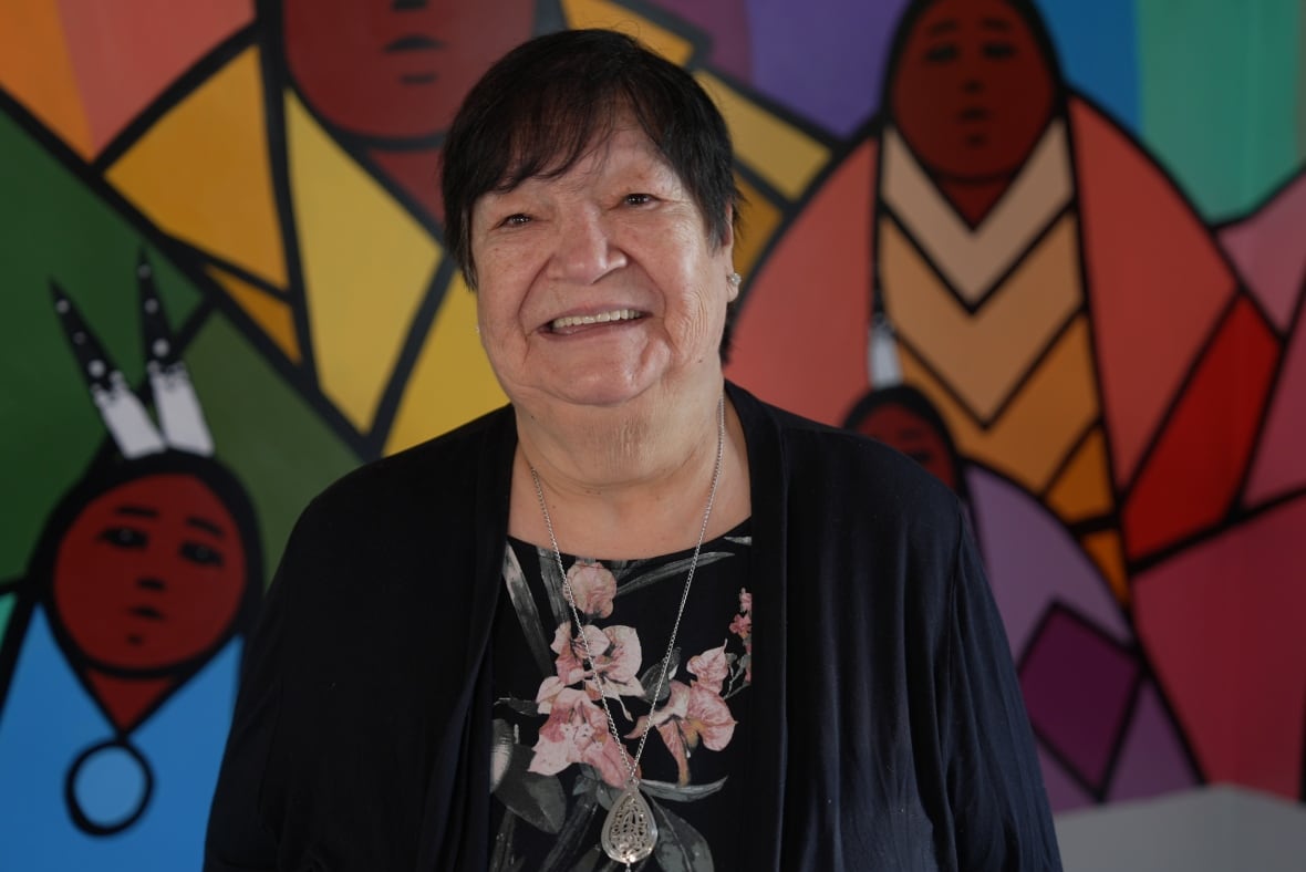 Smiling woman stands in front of colourful Indigenous artwork